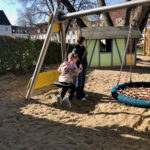 Erzieherin steht neben einem Kind auf der Schaukel