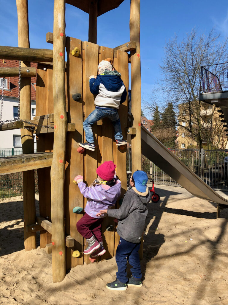 Drei Kinder erklimmen die Kletterwand des Klettergerüstes im Außenbereich